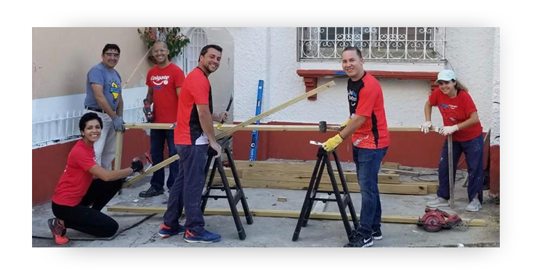Group of employee volunteers wearing red Colgate shirts with saw horses and tools standing in front of a building