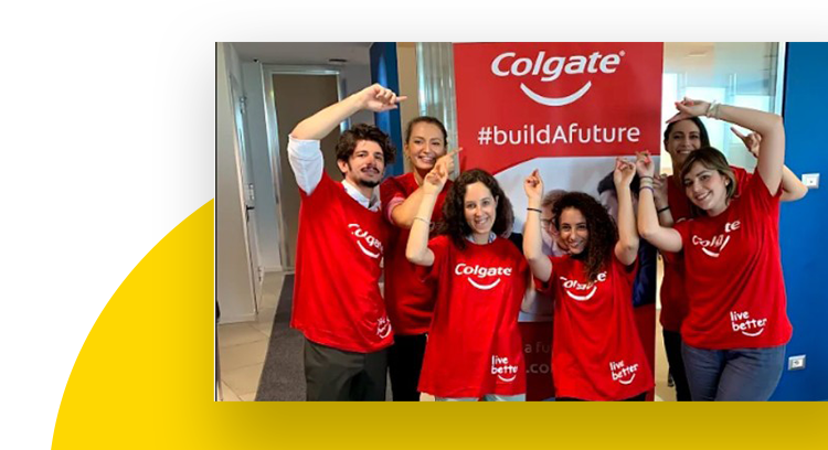 A group of employees wearing red Colgate Live better t-shirts smiling and pointing at a buildAfuture banner