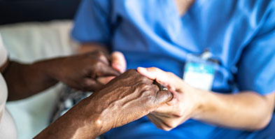 Close-up of caregiver and senior woman holding hands.