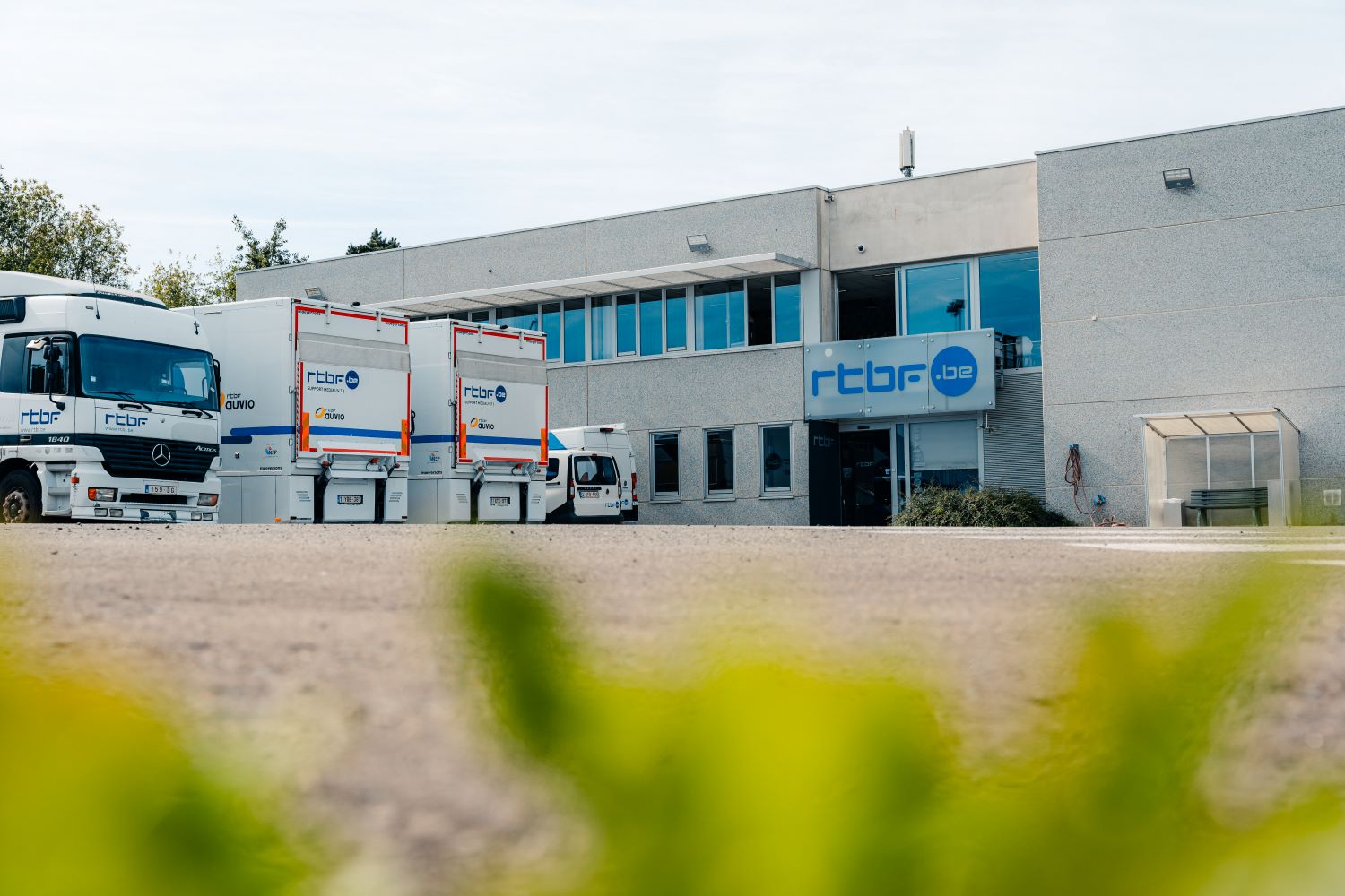 Photo d'un bâtiment RTBF devant lequel sont stationnés des poids lourds et camionnettes. 