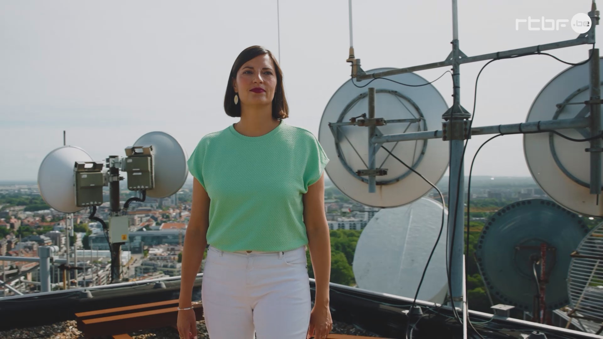 Sur le toit de la Tour Reyers, Justine, responsable éditorial investigation à la RTBF, prend la pose. Les antennes de diffusion sont visibles en arrière-plan.