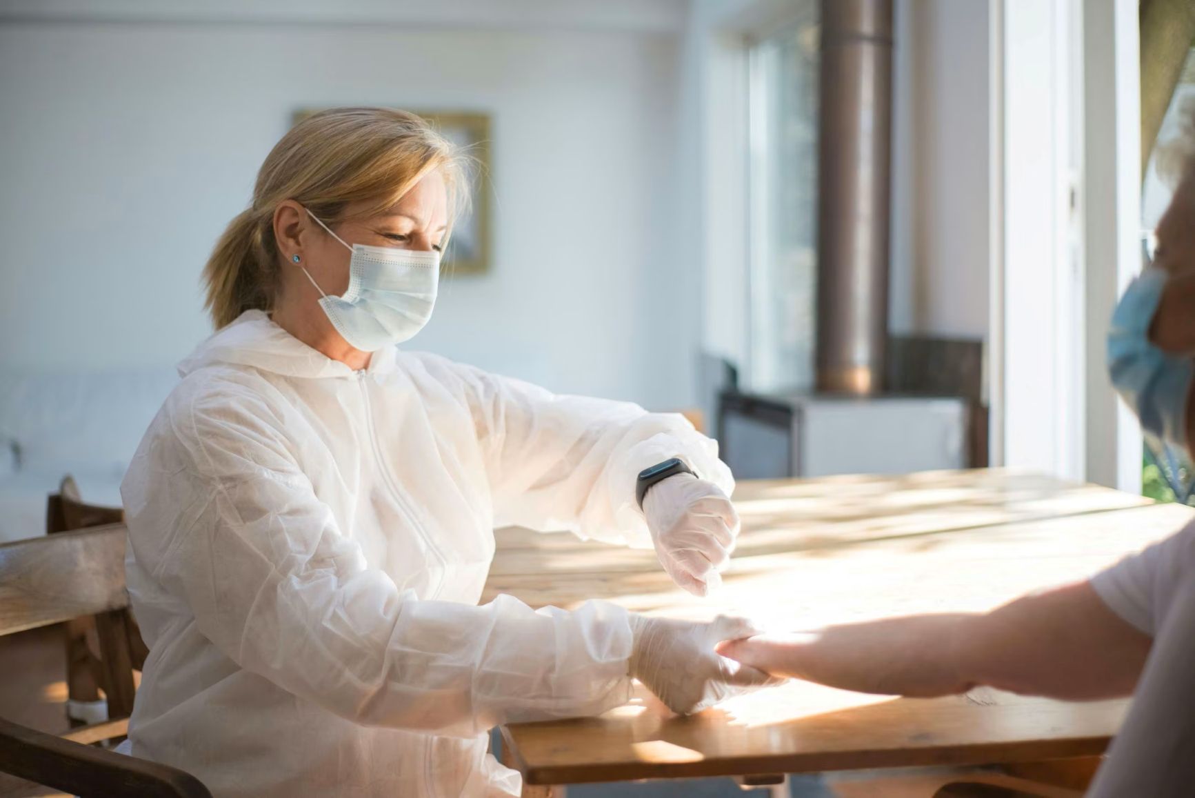 Healthcare worker in protective equipment examining a patient's hand during a consultation.
