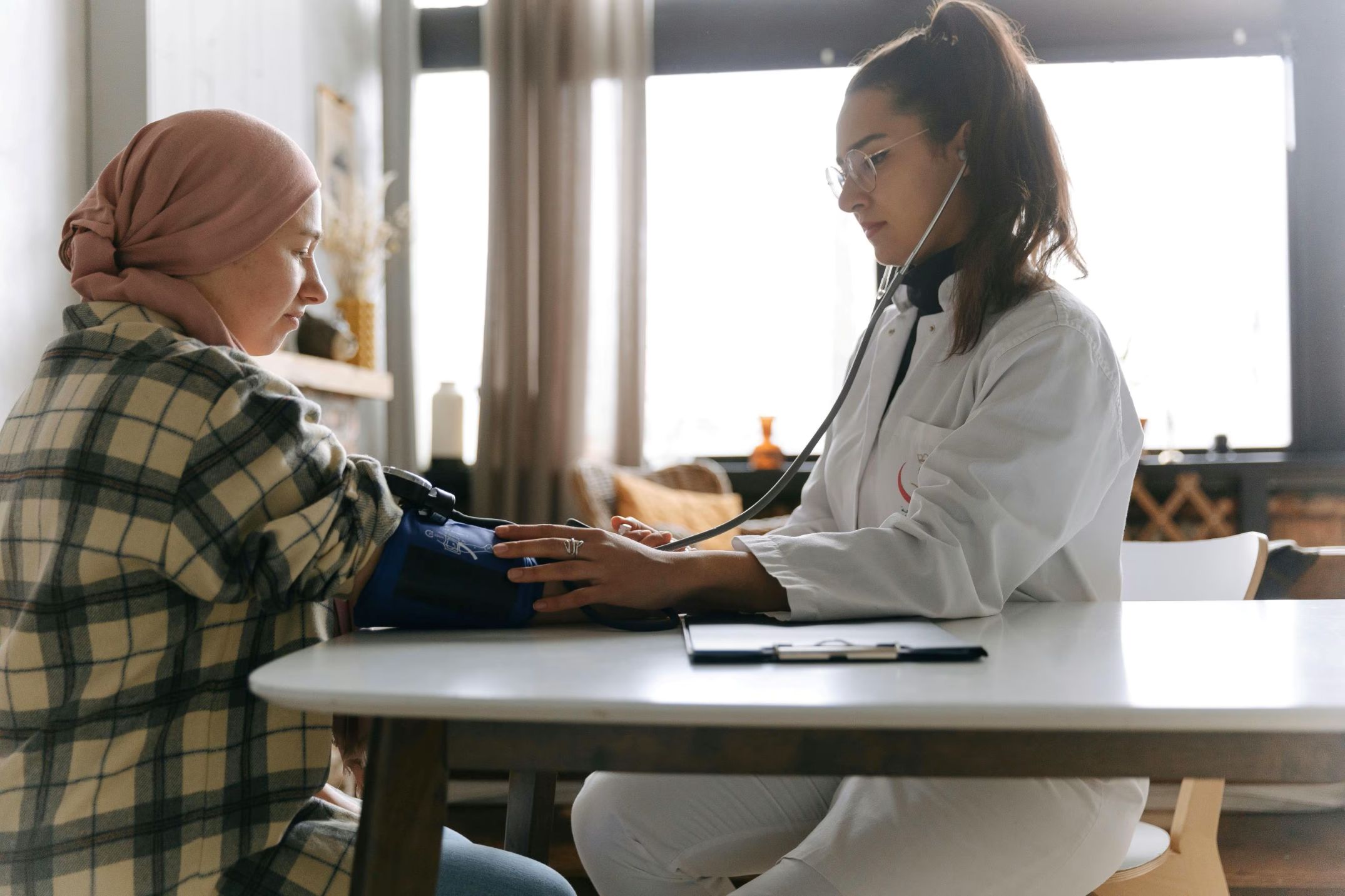 Healthcare professional measuring a patient's blood pressure during a consultation in a bright clinical setting.