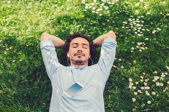 A man lying on the grass listening to music on his mobile phone
