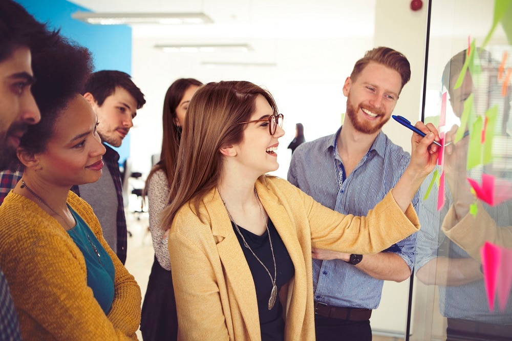 A woman writing a note on a whiteboard with others looking on