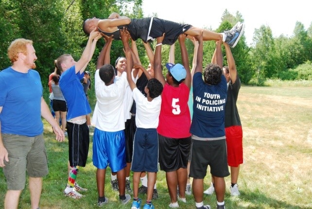 Group of youth outside, lifting their peer off the ground and into the air. 