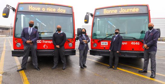 Photo de 4 employés se tenant devant deux autobus de la Ville d’Ottawa 