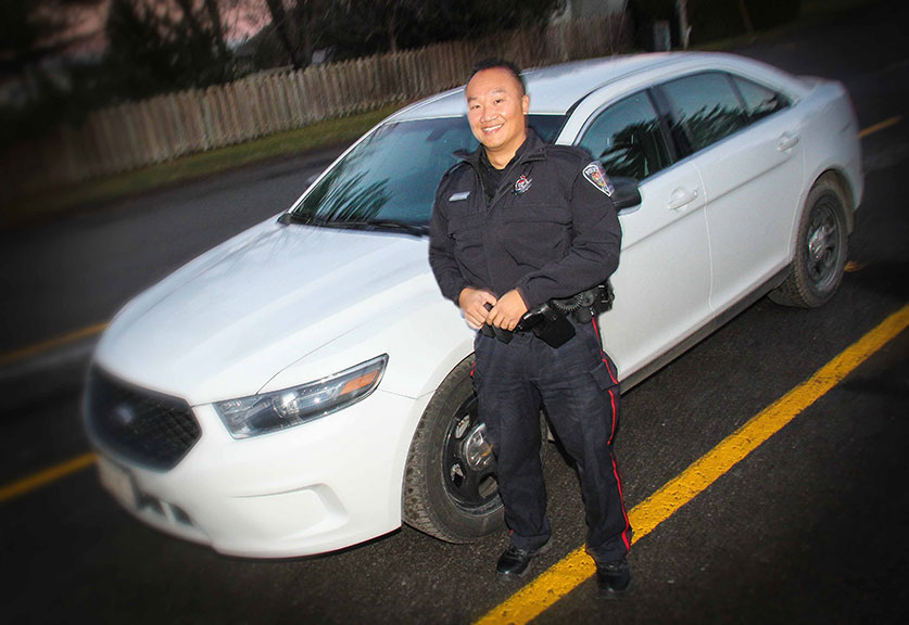 Male police officer standing beside his unmarked cruiser looking up at the camera.