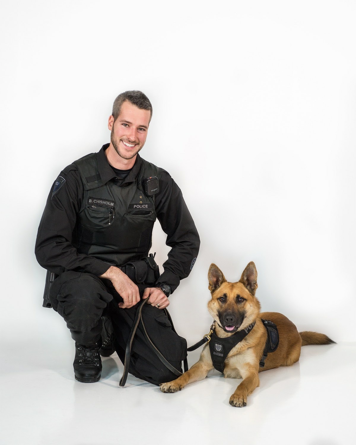 L'agent K9 du Service de police d'Ottawa à genoux à côté de son chien berger allemand qui est couché pour poser pour la photo.