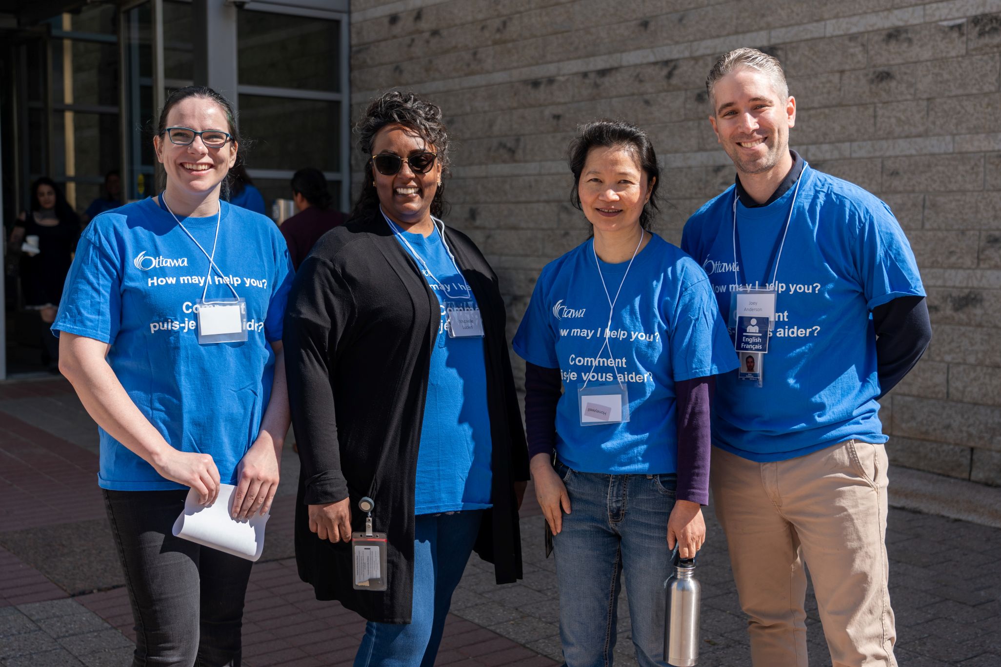 Four City of Ottawa employees standing in front of a building wearing blue shirts with the logo ‘How may I help you?’ support AccessAbility Day