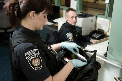 Une femme agent spécial fouille un sac à main tandis qu'un homme agent spécial est assis devant un ordinateur.