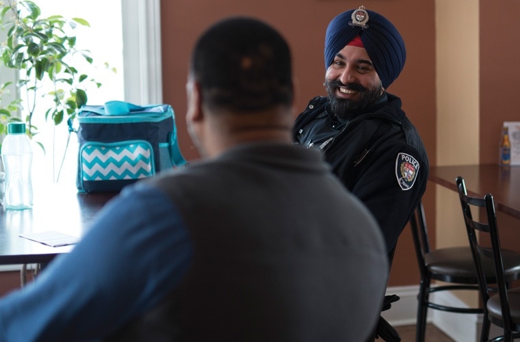 Smiling Ottawa Police Service officer sitting in a restaurant speaking to a member of the public