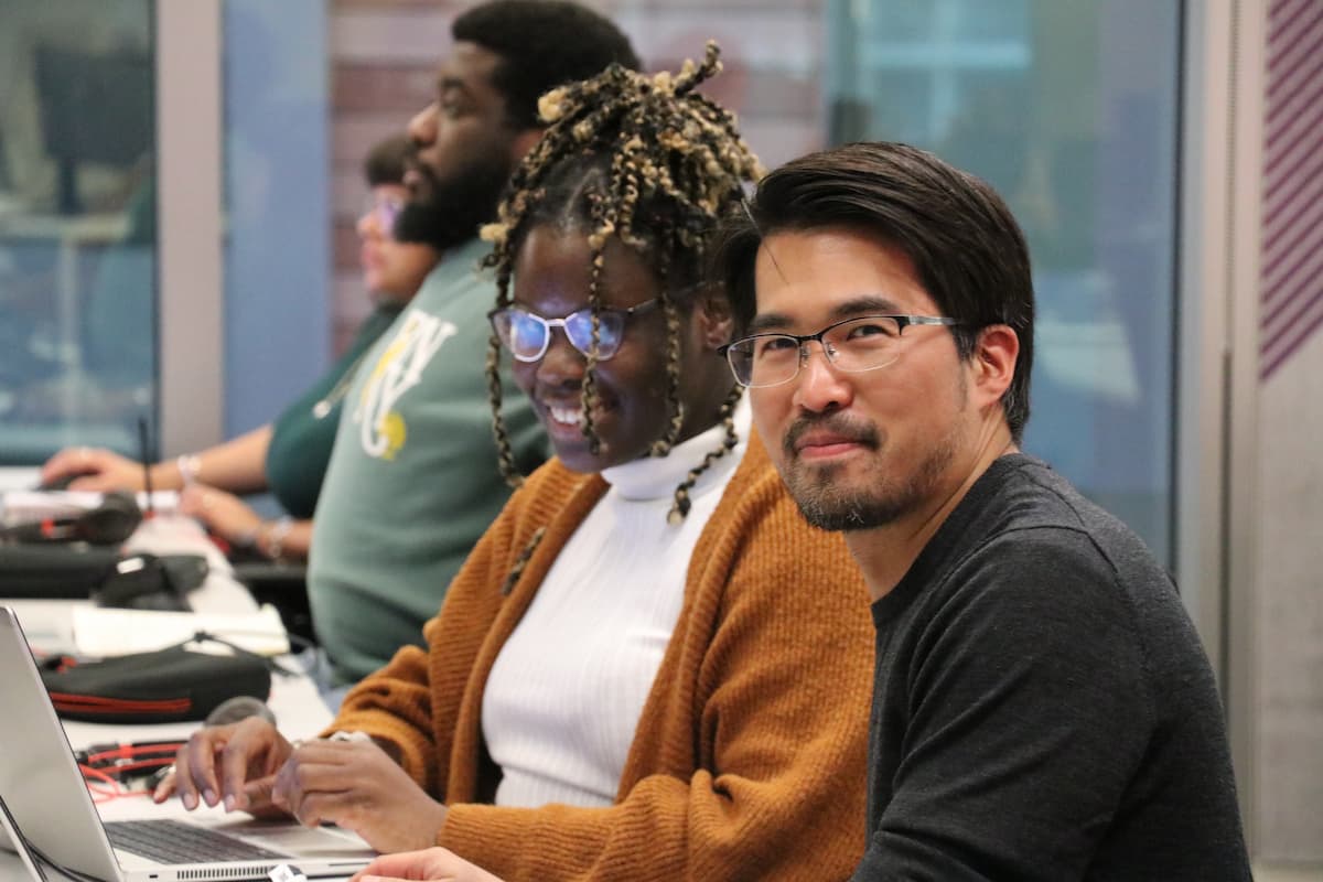 Two colleagues looking at the camera, smiling and working together at their desks