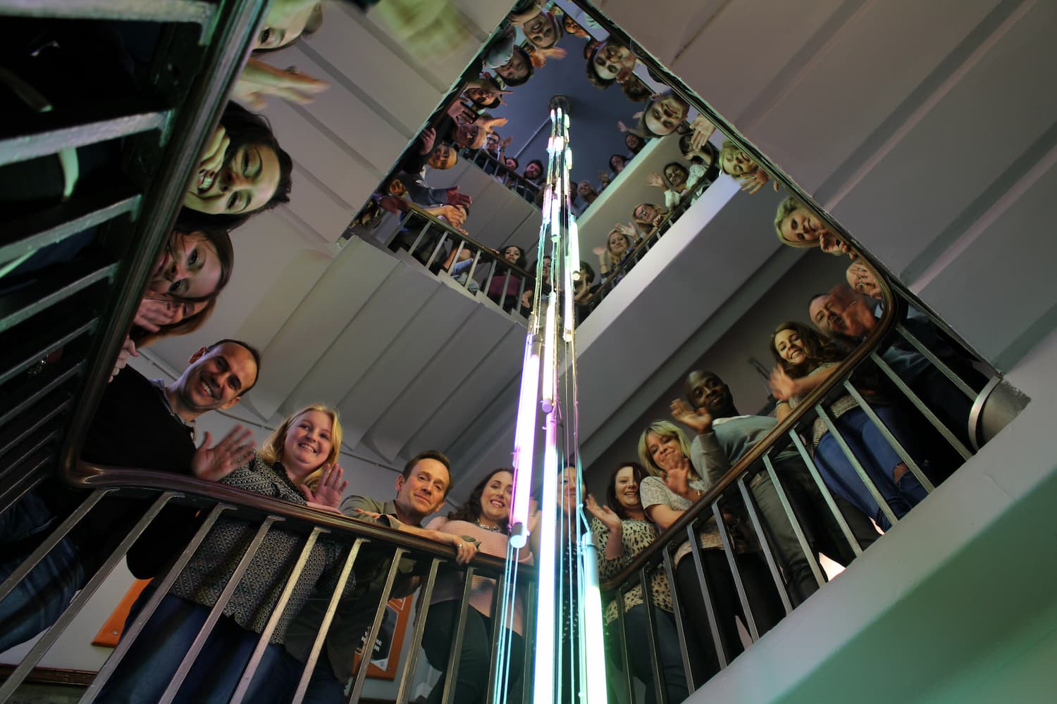 Agency staff gathered on three floors in a stairwell for a group shot, smiling and waving