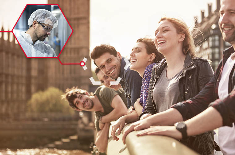 Een groep jonge mensen staat op een brug en kijkt blij en lachend voor zich uit.