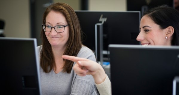 Two employees smiling and working together at computer workstation at WCB Nova Scotia’s office.
