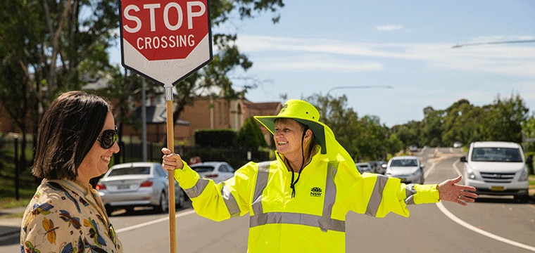 School Crossing Supervisor holding sign while pedestrians cross the road