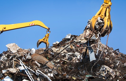 Two claws picking up scrap metal from a pile of scrap.