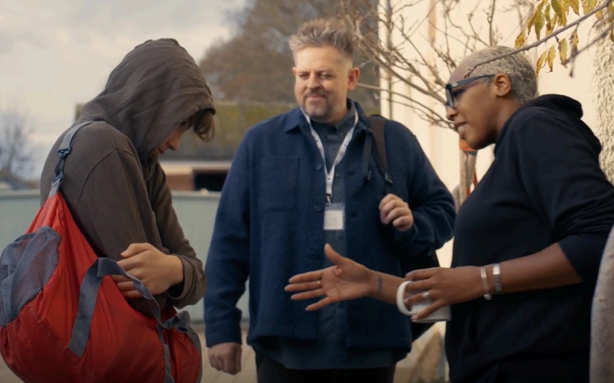 Three people talking outdoors near a building.