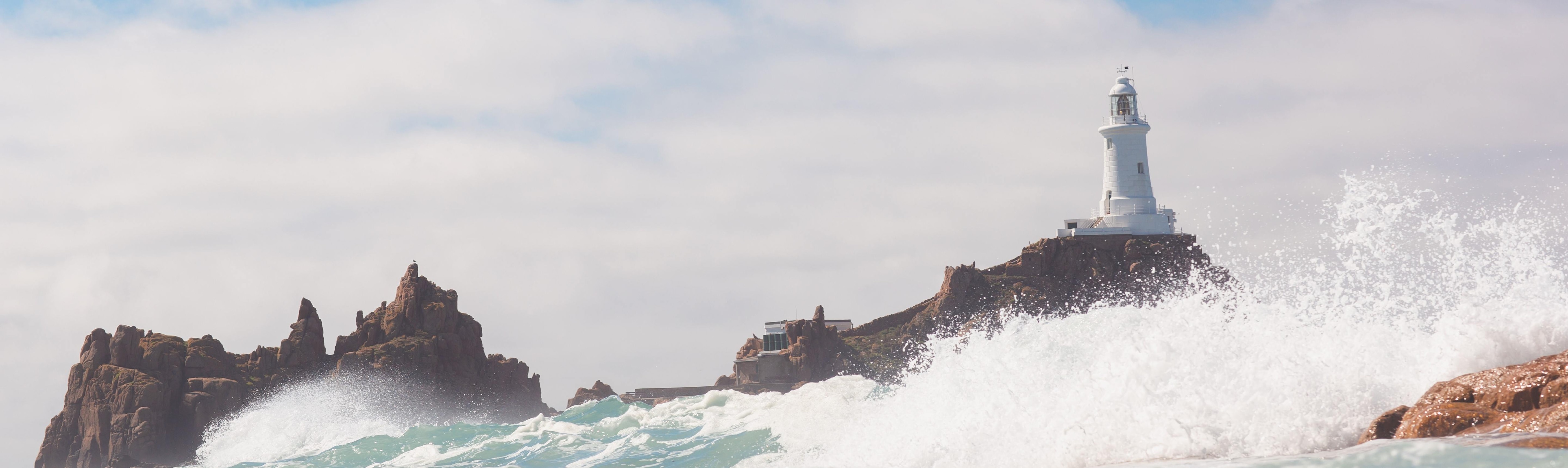 Banner image of La Corbière on a sunny, choppy day at high tide.