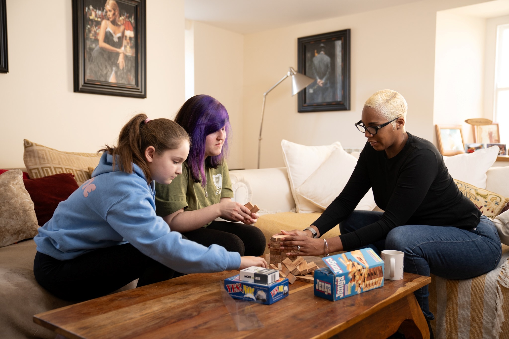 An adult and two young people sitting together around a table in a home setting playing a board game.