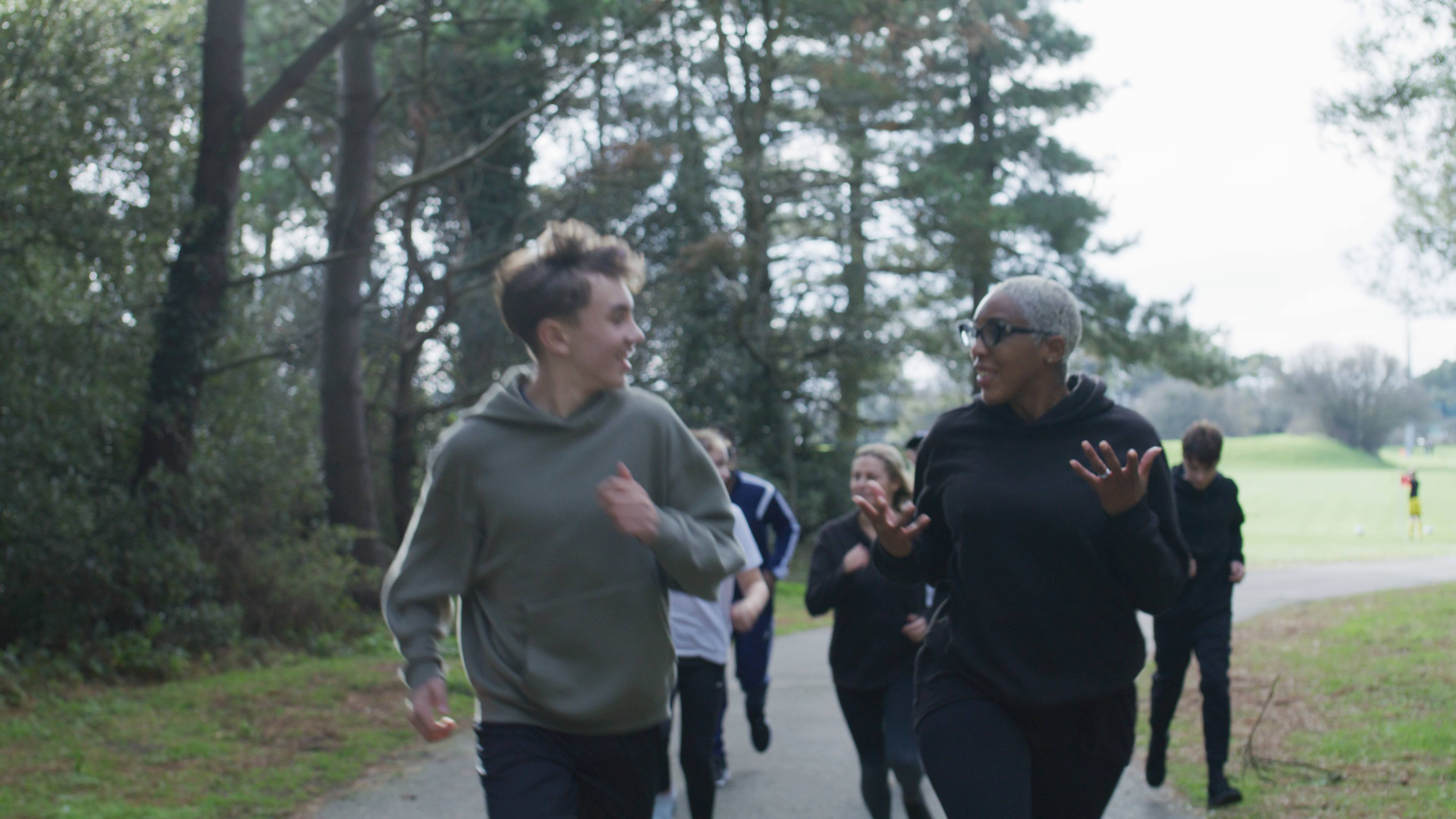 A group of people jogging along a path through a wooded area.