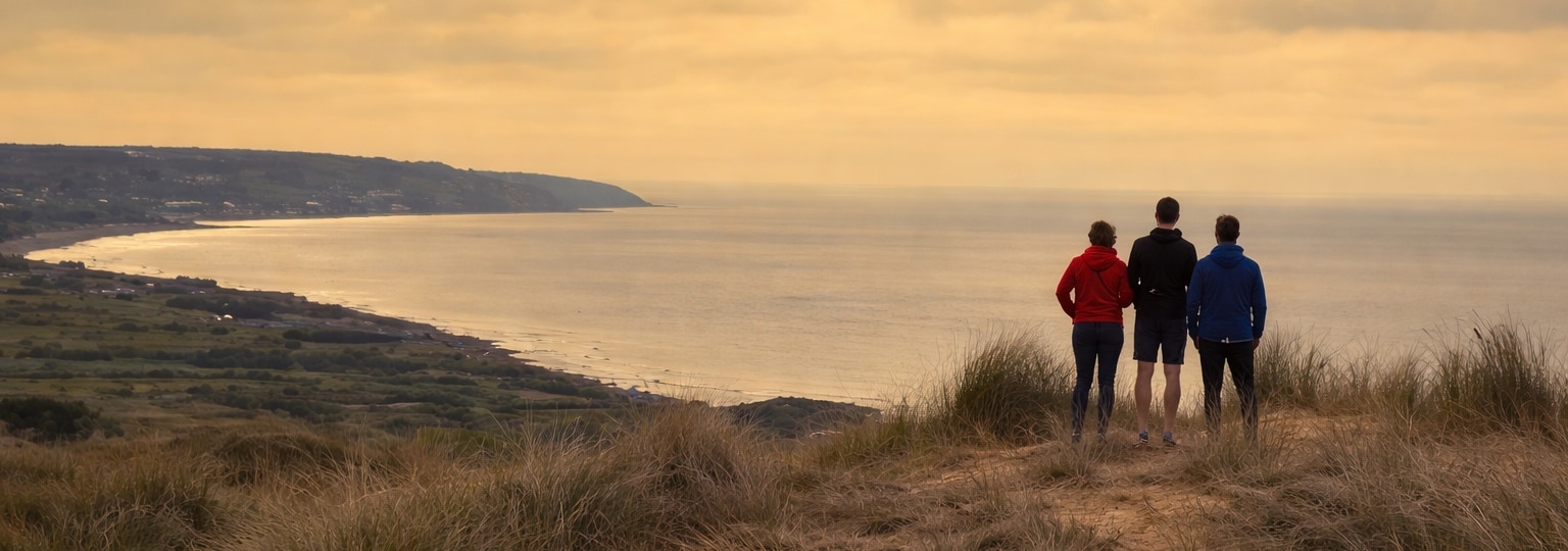 Three people standing on a coastal headland overlooking the sea.