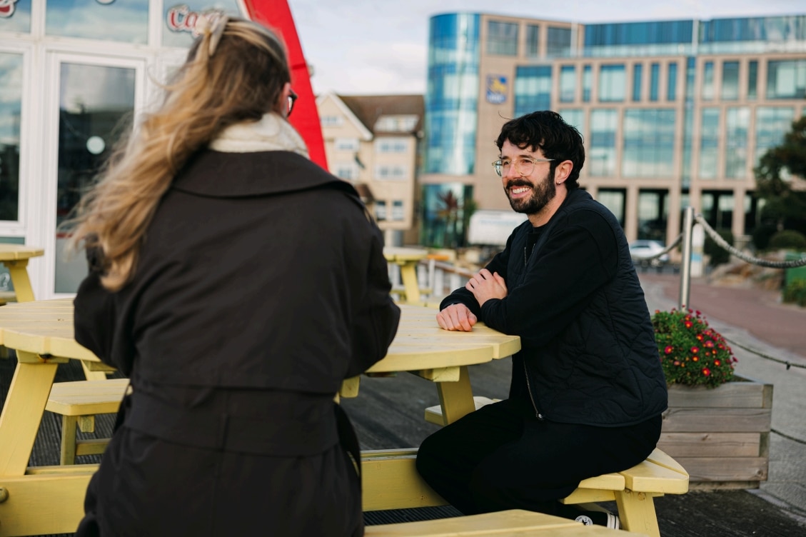 Two people talking while seated at an outdoor table.
