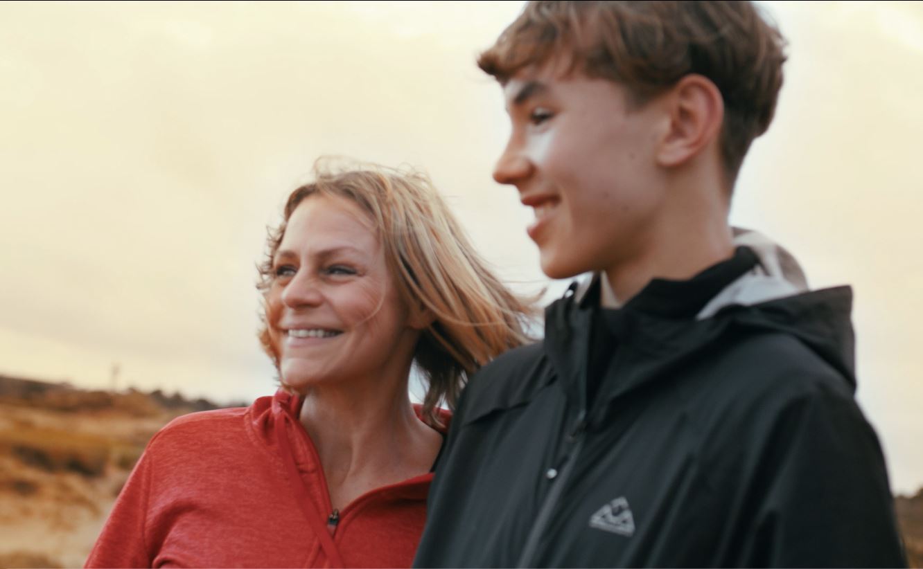 A woman and a boy smile together outdoors