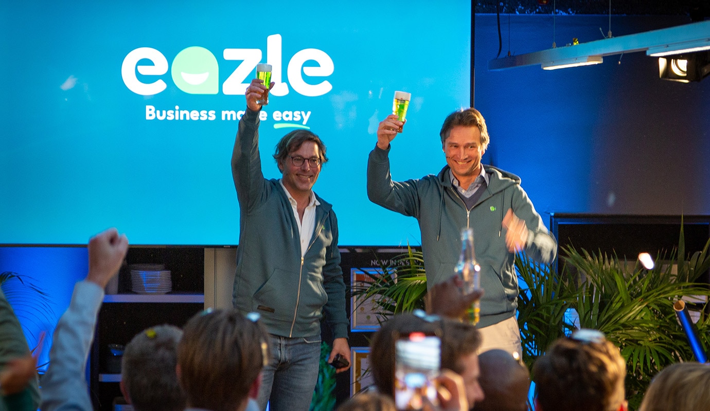 Two colleagues on stage raising a glass of Heineken as they present to colleagues, with a screen in the background displaying HEINEKEN's B2B platform "Eazle: Business made easy".