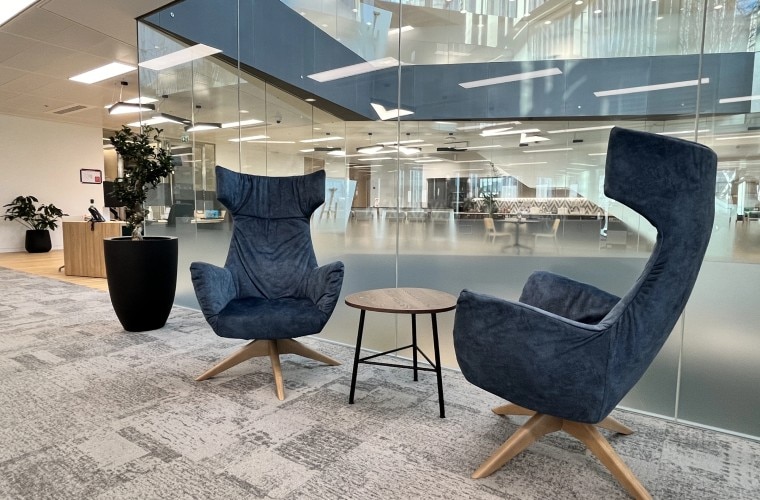 Two chairs and a small table in front of a glass wall with a potted plant.