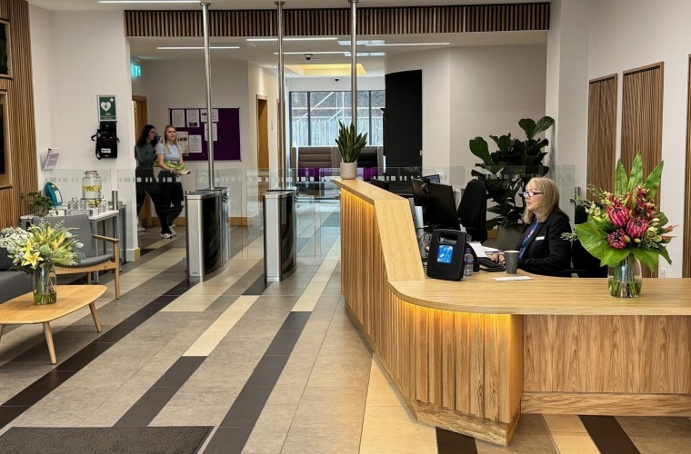 A reception desk with security barriers, with fresh flowers on the counter.