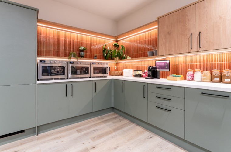 A kitchen with green cupboards, stylish lighting and facilities to heat food.