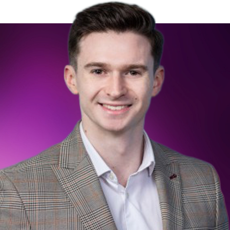 A colleague wearing a white shirt under a blazer against a purple background, they are smiling.