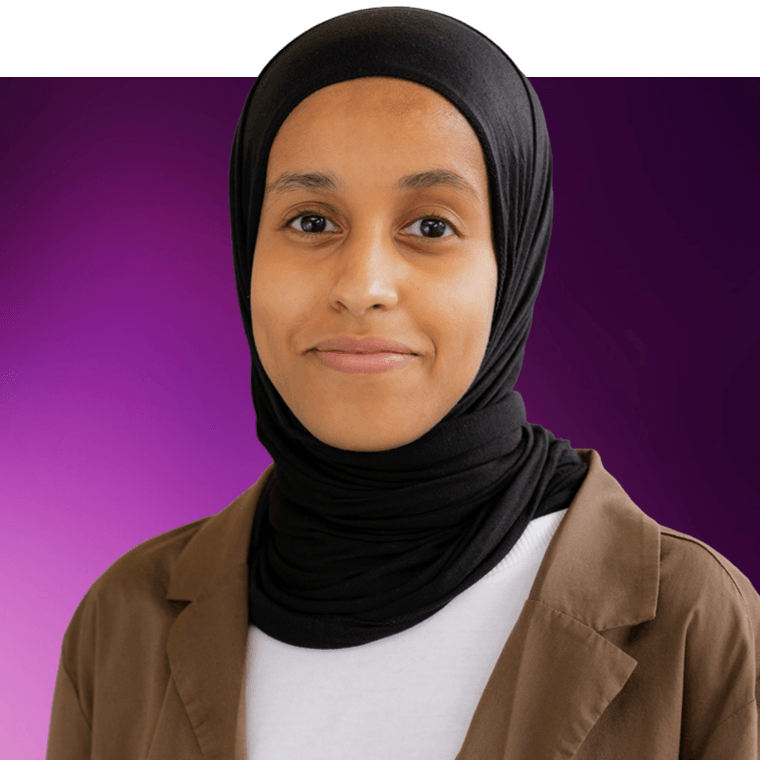 A colleague wearing a hijab and a brown blazer over a white shirt, they are smiling.