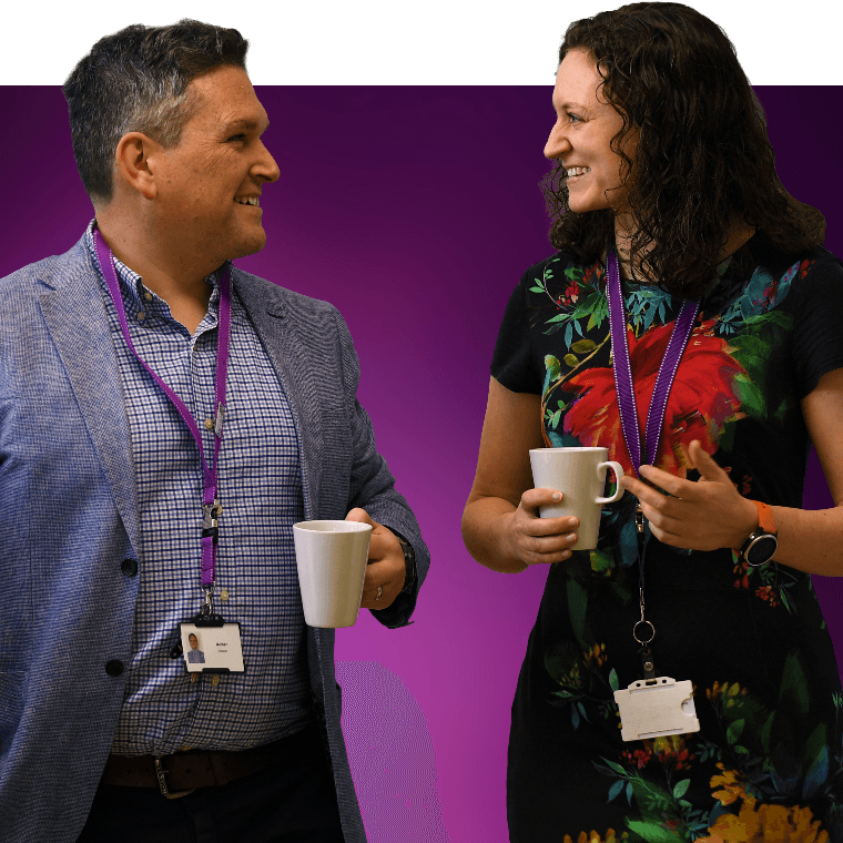 Two colleagues walking and talking with hot drinks.