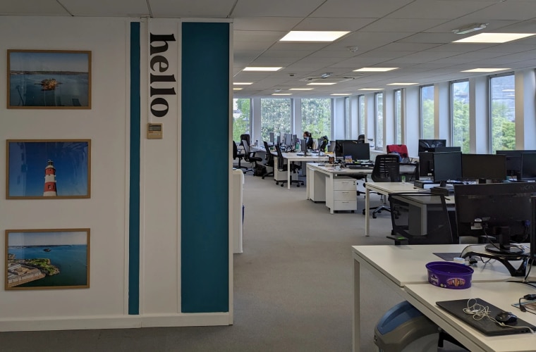 An office with desks and a teal coloured wall with the word hello on it.