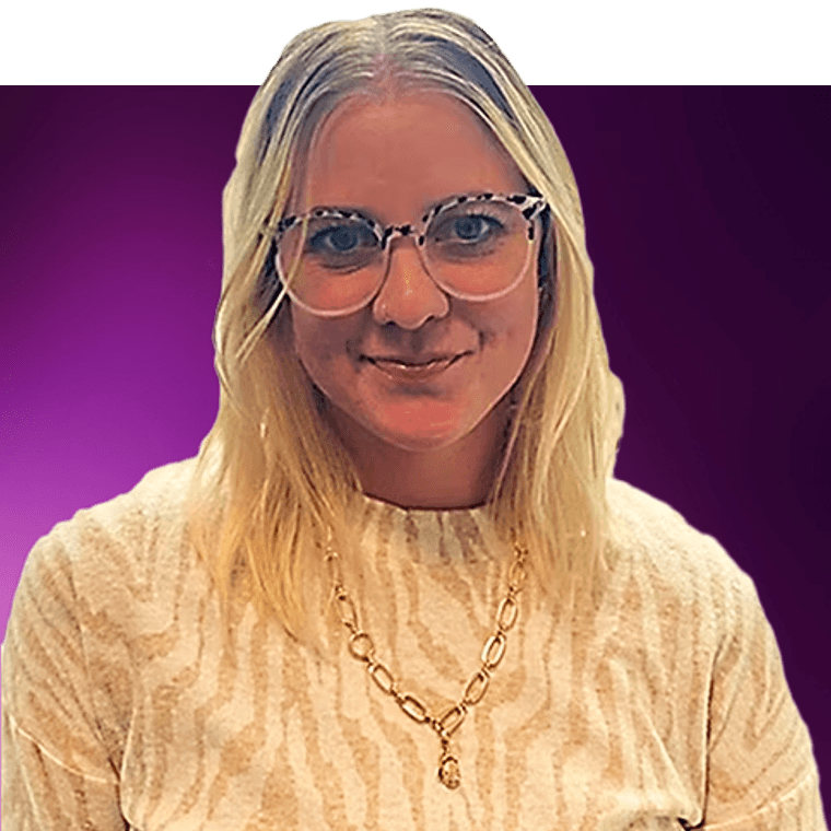 A colleague with blonde coloured hair wearing animal print glasses and a beige animal print jumper under a gold necklace.