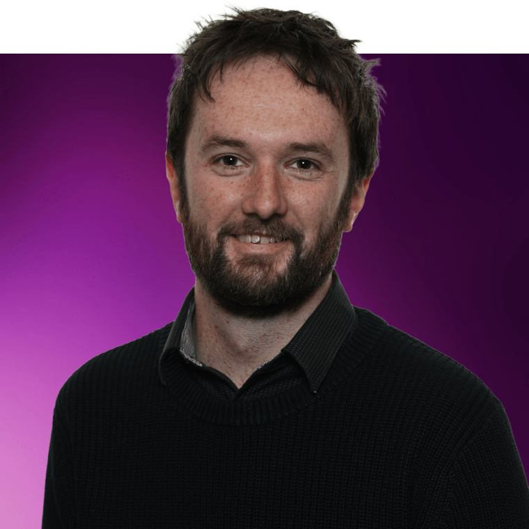 A colleague with brown coloured hair and a beard, wearing a dark coloured jumper of a shirt.