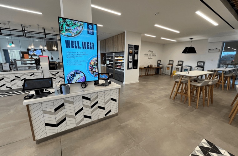 A restaurant with a serving counter, tills, screens, fridges and seating.