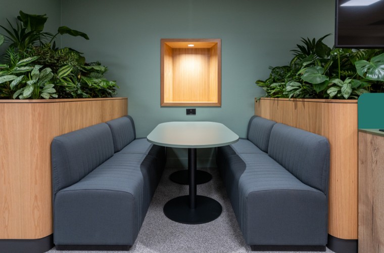 A seating booth with a green background wall and plants on either side.