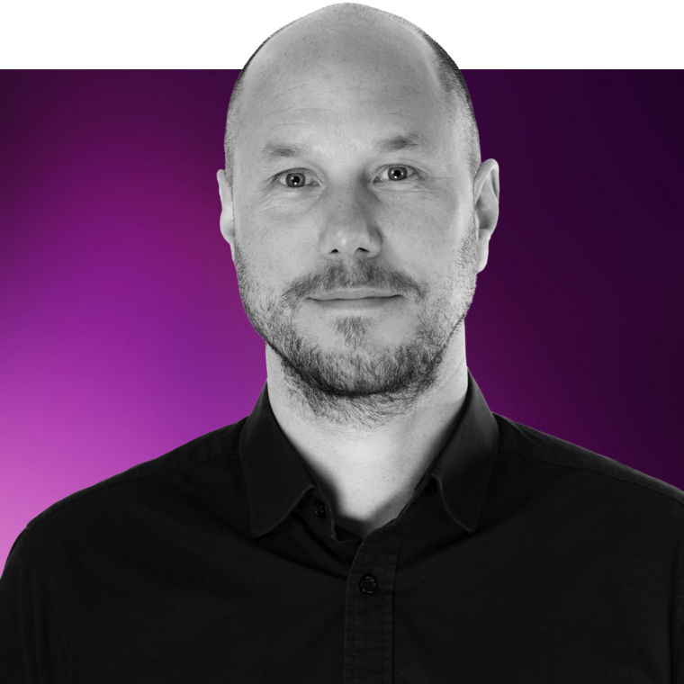 A black and white photo of a colleague with a beard, wearing a black shirt on a purple background.