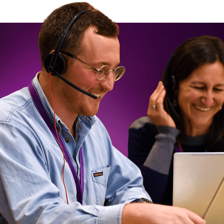 Two colleague sat at a laptop on a Teams call, smiling.