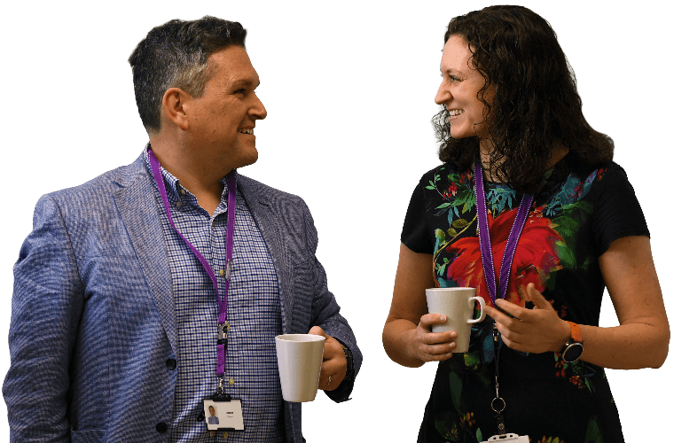 Two colleagues walking and talking with hot drinks.