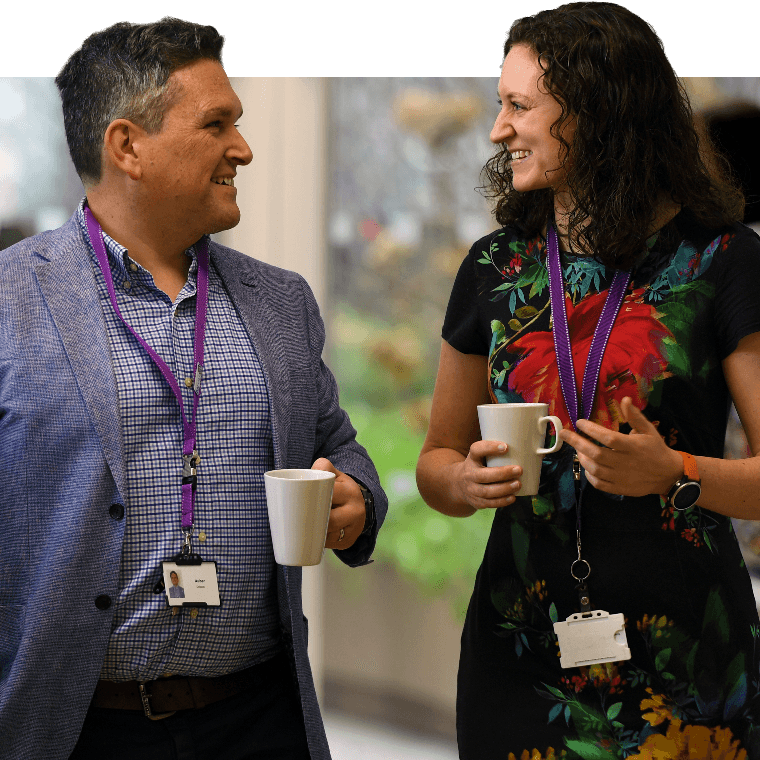 Two colleagues walking and talking with hot drinks.