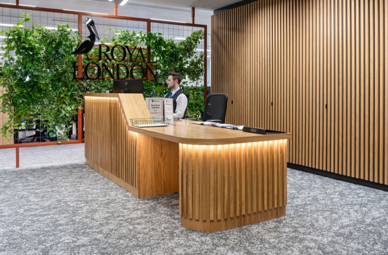 A reception desk made of wood in front of a living wall of plants with the Royal London logo.