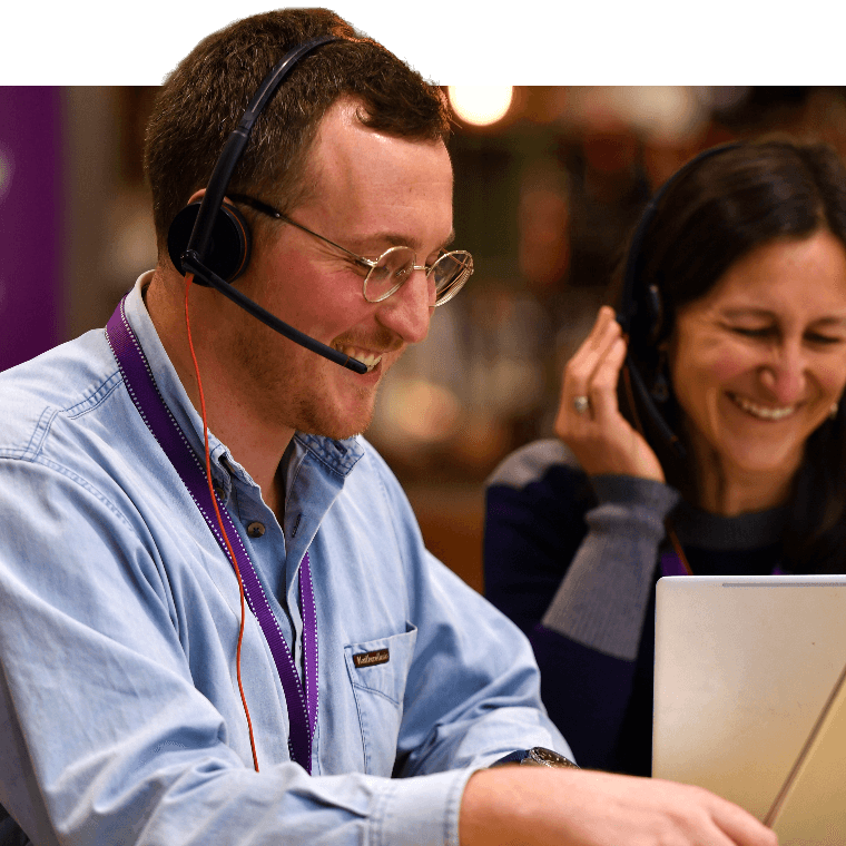 Two colleague sat at a laptop on a Teams call, smiling.