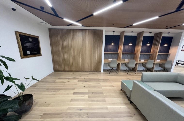 An open plan workspace with wooden panelling on the walls and small desks and a large grey sofa.