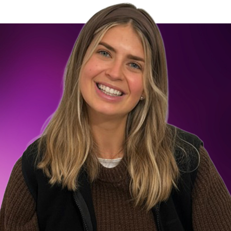A colleague with light coloured hair wearing a brown jumper under a black sleeveless top against a purple background, they are smiling.