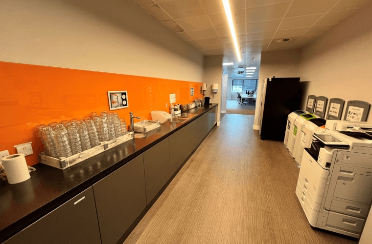 A long kitchen with a vibrant orange splash back.